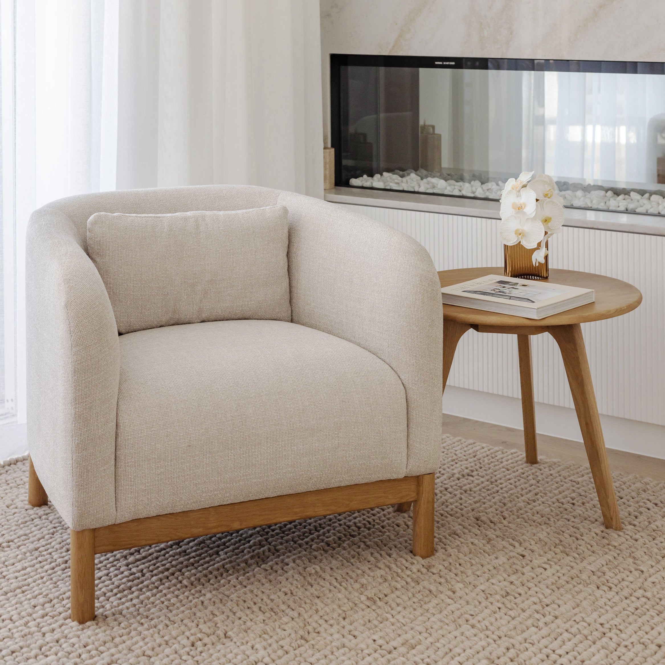 Beige armchair in a living room with a side table and fireplace.